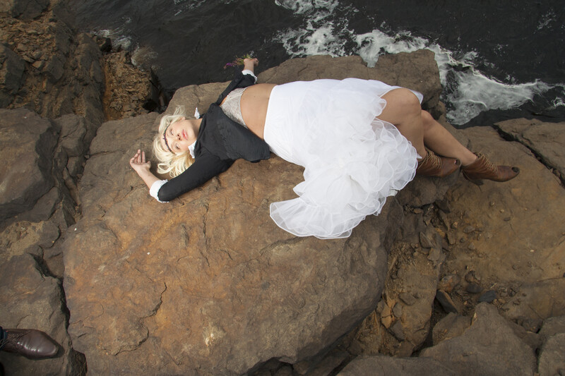 Woman in white dress lying on rocky coastal outcrop above dark ocean water.