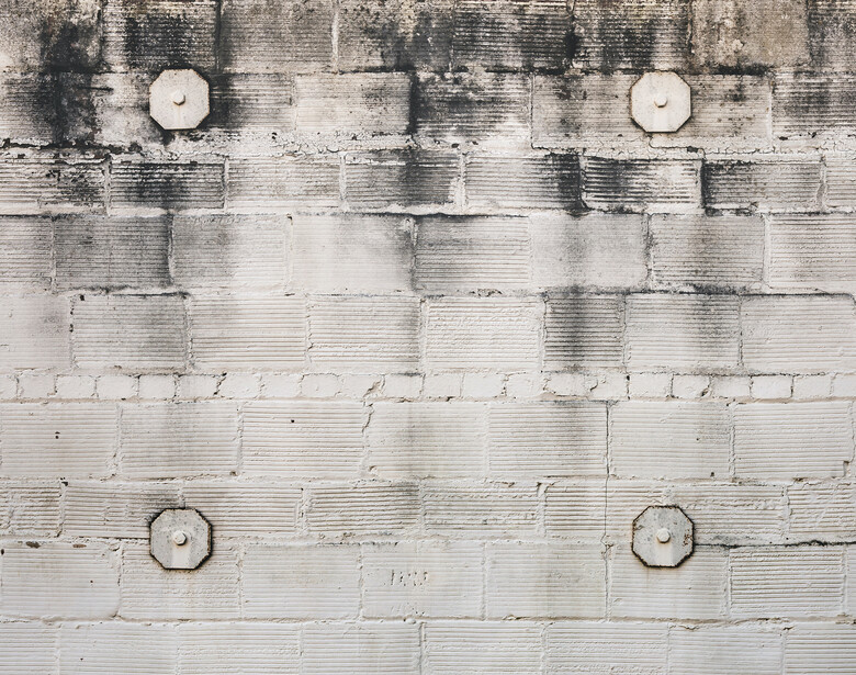 Overhead view of a weathered white brick wall with four circular vents symmetrically arranged and water stains.