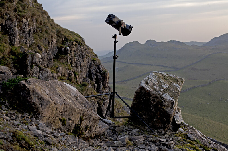 Professional lighting rig mounted on rocky outcrop overlooking mountainous valley.