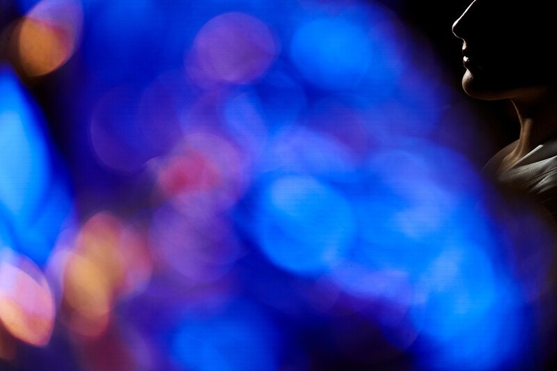 Profile silhouette of a person against a vibrant, blurred bokeh background of blue and purple lights.