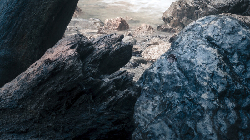 Rocky boulder formations casting deep shadows in an arid, desert-like landscape with distant rock formations.