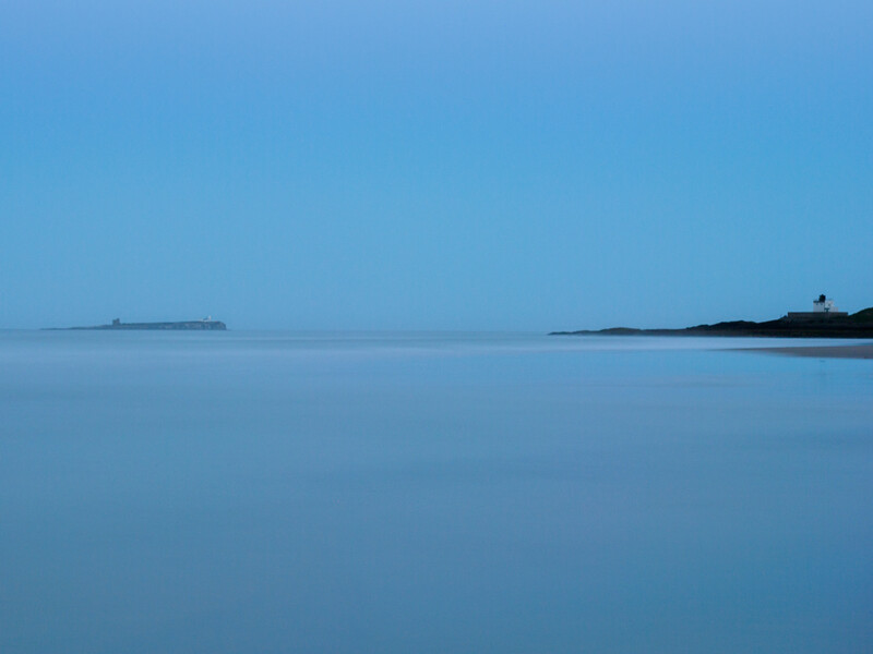 Calm seascape with distant islands under clear blue sky at twilight or dawn.