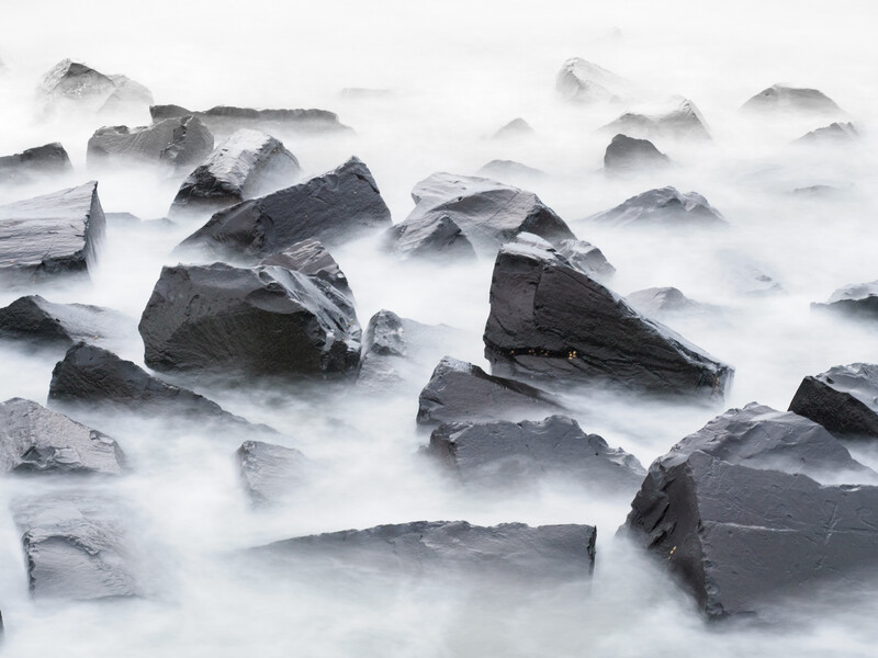 Dark rocks emerging from silky white water created by long exposure photography.