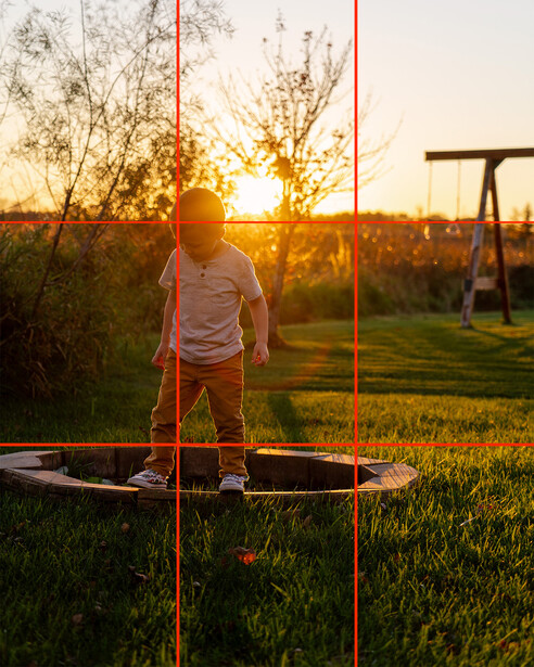 Child standing on trampoline during golden hour with rule-of-thirds grid overlay.