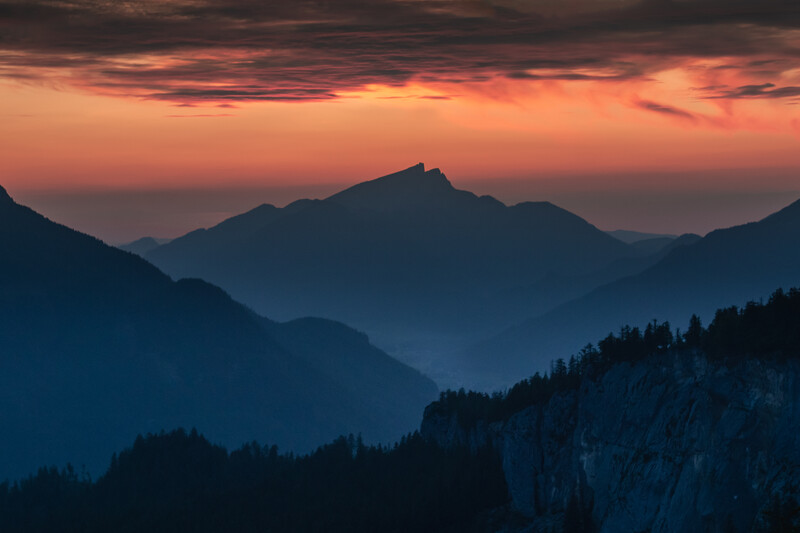 Layered mountain silhouettes at sunset with golden-orange sky and deep blue foreground ridges.