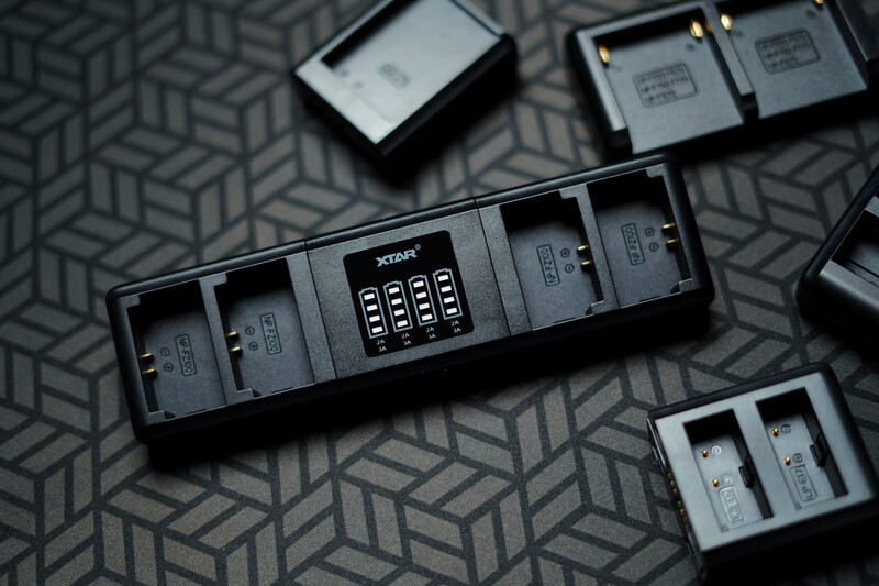 Xtar MC4 battery charger with four charging slots and digital display, surrounded by loose batteries on a patterned surface.