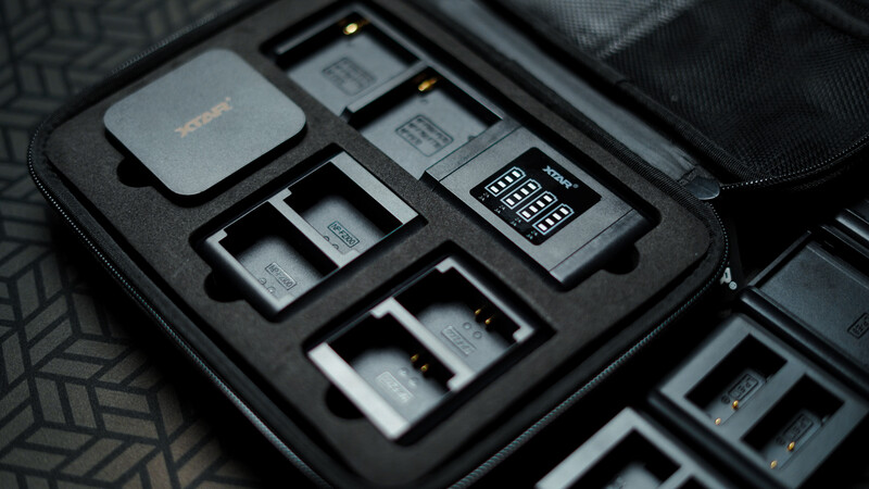 Organized camera gear storage case with batteries, memory cards, and accessories neatly arranged in foam inserts.