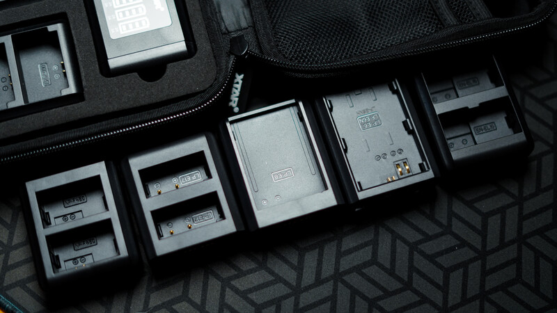 Collection of white battery holders and storage cases organized in a padded black travel bag.