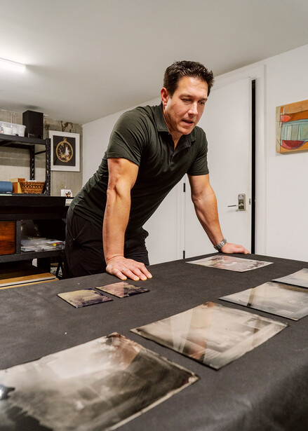 Photographer reviewing contact sheets and prints at a workspace table with natural studio lighting.