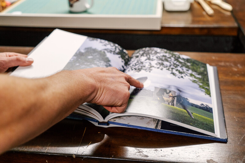 Person's hands turning pages of a printed photo book on a wooden desk.