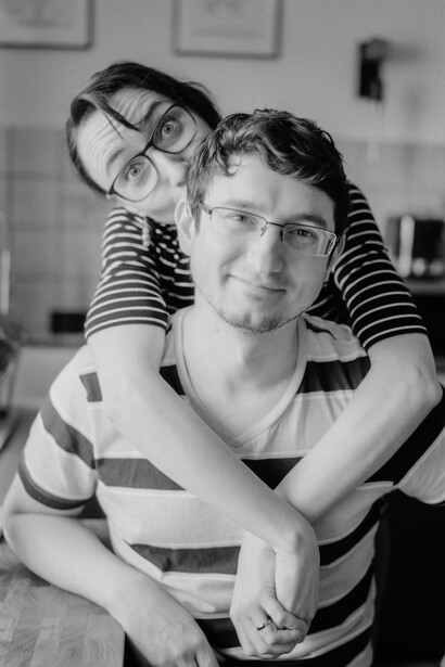 Adult man wearing striped shirt with child's arms around his shoulders, both wearing glasses, black and white portrait.