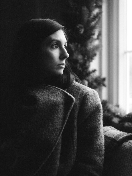 Woman in profile looking toward a window, wearing a textured sweater in a high-contrast black and white portrait.