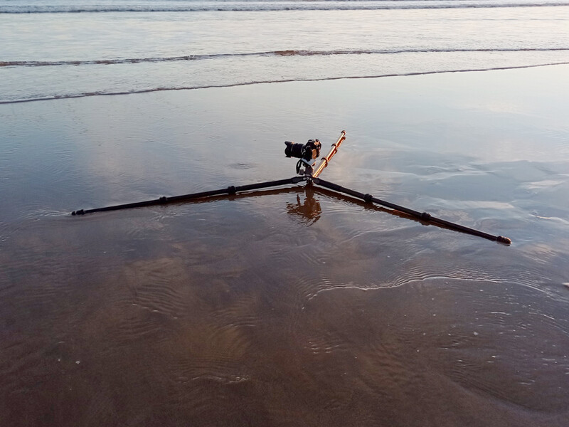 Jib crane with extended boom reflected in still water during golden hour light.