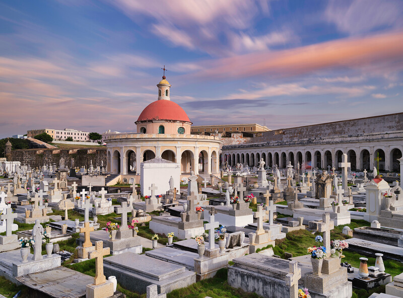 Cemetery with white tombstones and a domed chapel with red roof at sunset.