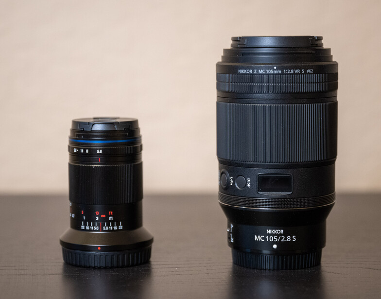 Two black camera lenses of different sizes arranged side by side on a surface against a neutral beige background.
