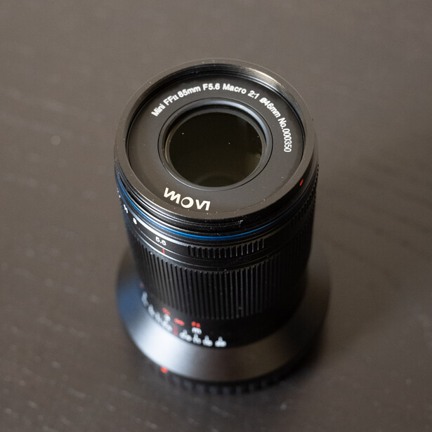 Telephoto lens mounted vertically showing rear element and focus ring against neutral background.