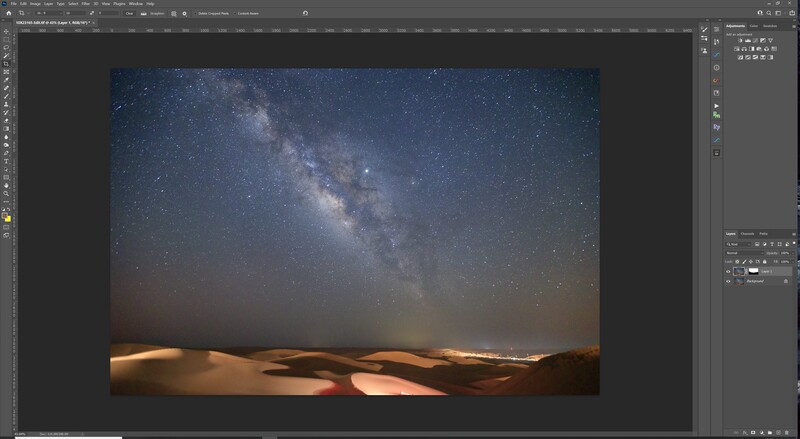 Milky Way galaxy stretches across a starry night sky above illuminated sand dunes.