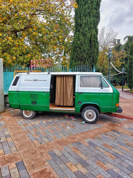 Vintage green and white camper van parked on brick pavement with autumn trees in the background.