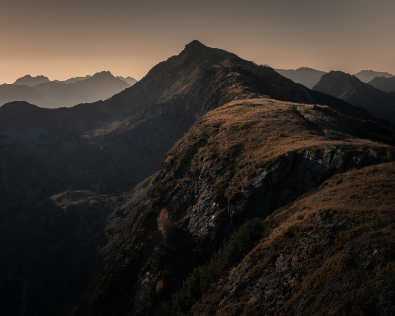 Rocky mountain ridge silhouetted against a hazy golden-brown sky at dusk or dawn.