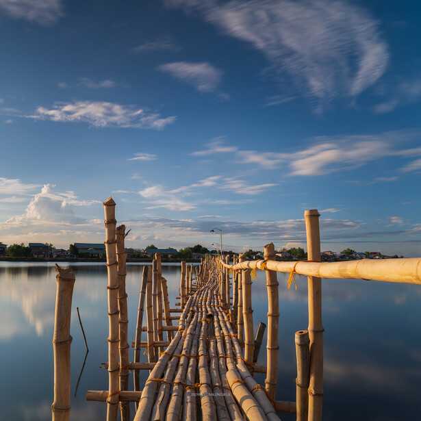 Wooden boardwalk extending into still water with perfect mirror reflections under a blue sky.