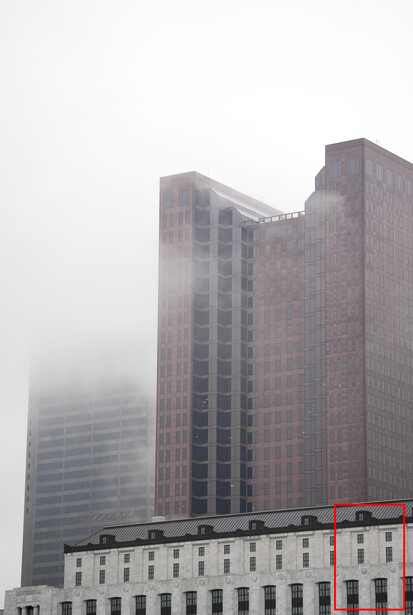 Tall residential towers partially obscured by dense fog, with a lower classical building in the foreground.