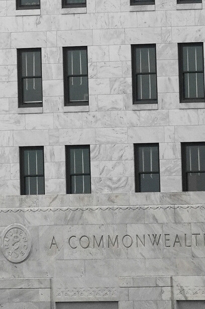 Symmetrical facade of a stone government building with rows of tall windows and carved text reading "A COMMONWEALTH."