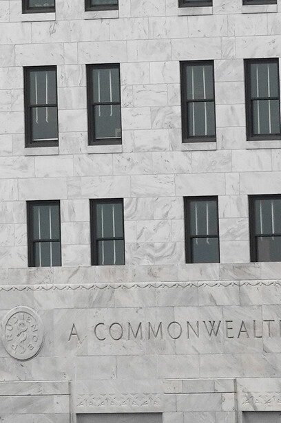 Symmetrical facade of a stone building with eight tall windows arranged in two rows and text reading "A COMMONWEALTH" carved into the lower section.