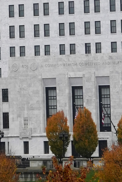 Neoclassical government building facade with symmetrical windows and stone columns flanked by autumn foliage.