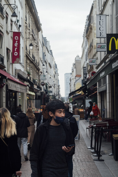 Pedestrians walking down a wet European shopping street lined with storefronts and signage.