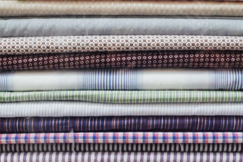 Stack of fabric swatches with various woven patterns and stripe designs in neutral, brown, blue, and green tones.