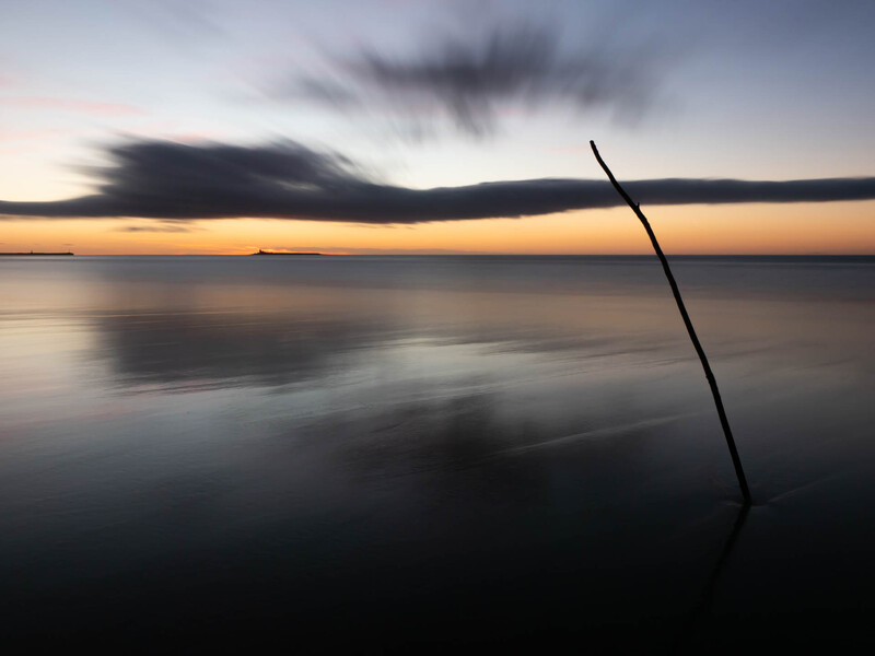 Tilted wooden post emerging from still water at dusk, silhouetted against a golden and purple sky.