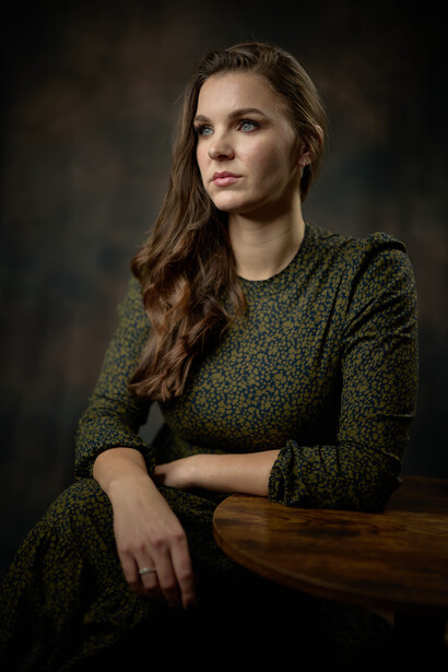 Woman in dark green knit sweater gazing to the side against dark background.