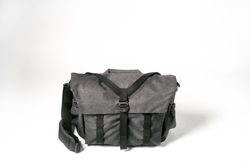 Gray and black canvas camera bag with flap closure and shoulder strap against white background.