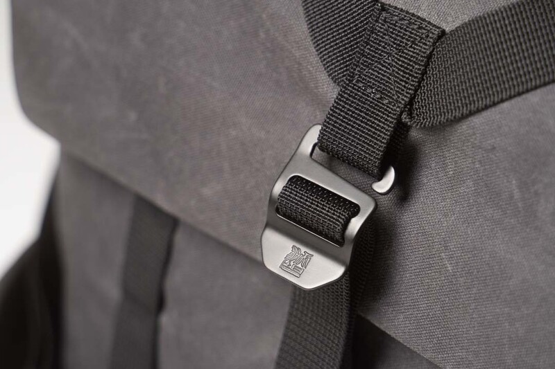 Close-up of a metal side-release buckle attached to black webbing on gray fabric.