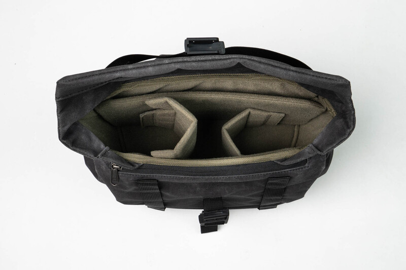 Black camera bag with open top showing beige dividers and compartments for equipment storage.