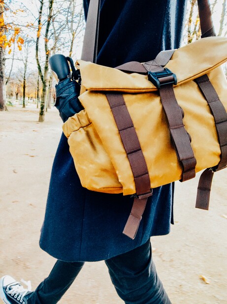 Person wearing a mustard-yellow canvas messenger bag with brown leather straps over a dark blue coat.