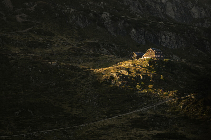 Illuminated mountain cabin nestled in a dark forested valley surrounded by steep rocky cliffs.