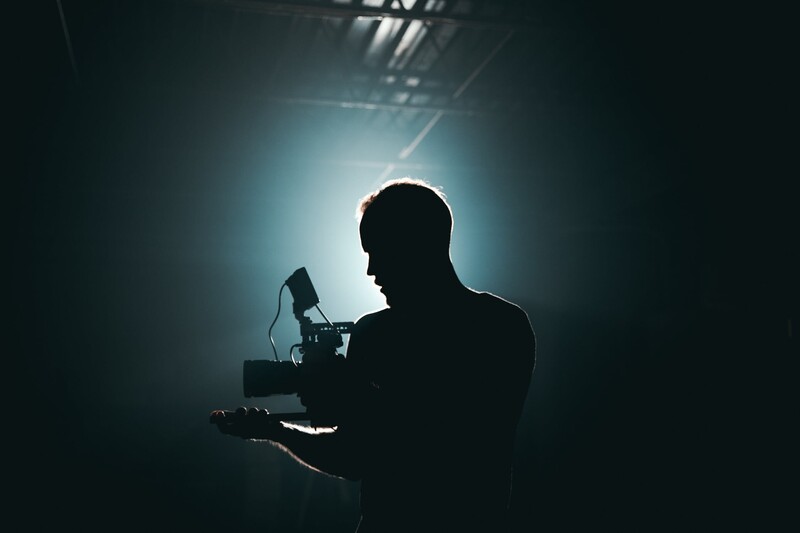 Silhouetted figure operating camera equipment against backlit glow.