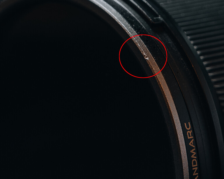 Close-up of a camera lens barrel showing dust or debris circled in red on the glass surface.
