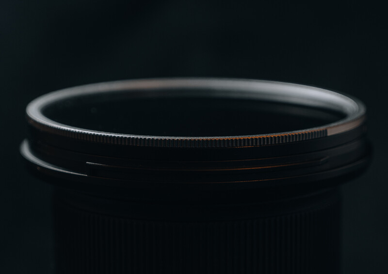 Camera lens filter with metal rim and serrated edge ring against dark background.