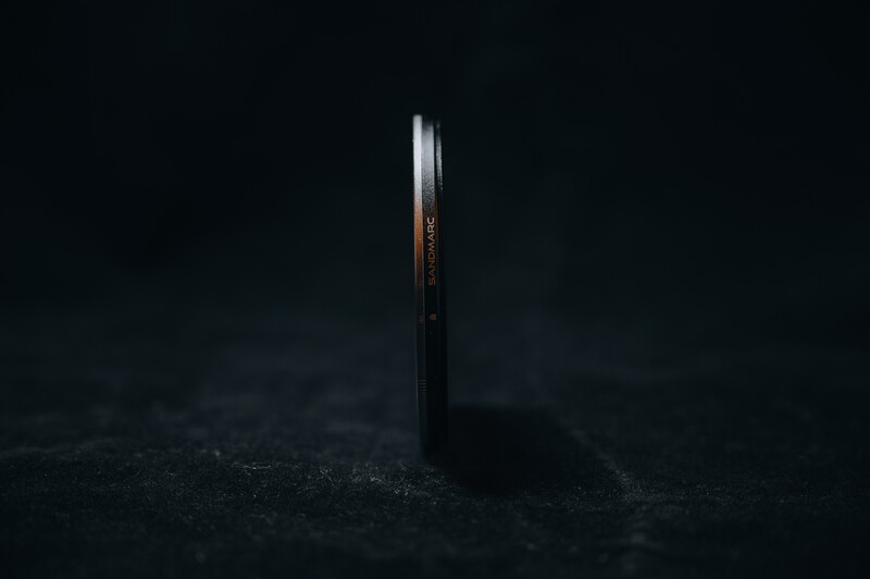 A lens standing upright on dark ground against a black background, with light reflecting off its barrel.