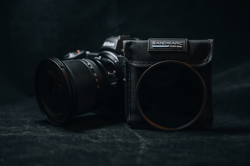 Professional camera with attached lens next to a square filter holder with circular filter on dark textured surface.