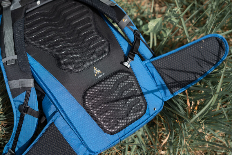 Blue and black camera bag with padded dividers laid flat on grass, showing interior organization compartments.