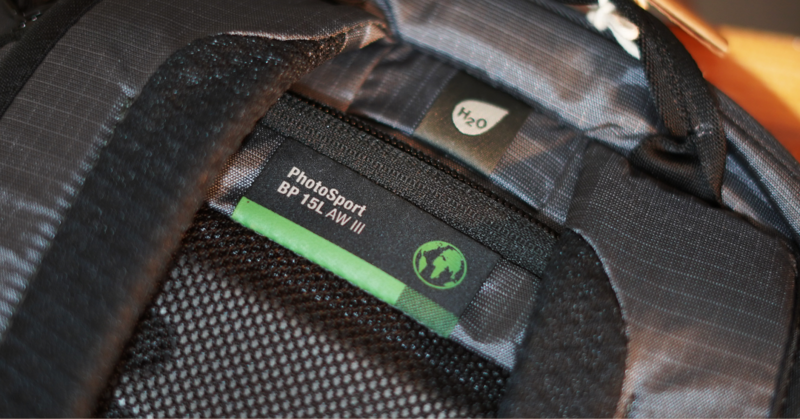 Close-up of camera gear showing a protective bag with mesh ventilation and branded label with green accents.