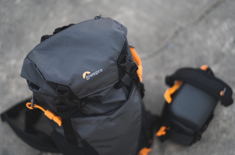 Lowepro camera backpack with blue body and orange accents displayed overhead on concrete surface.