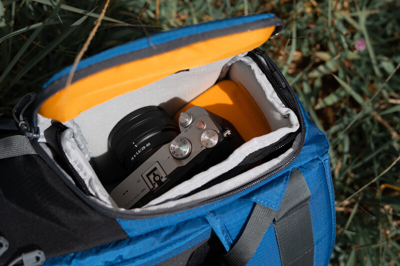 A compact camera and lens nestled in protective foam inside a blue and yellow camera bag.