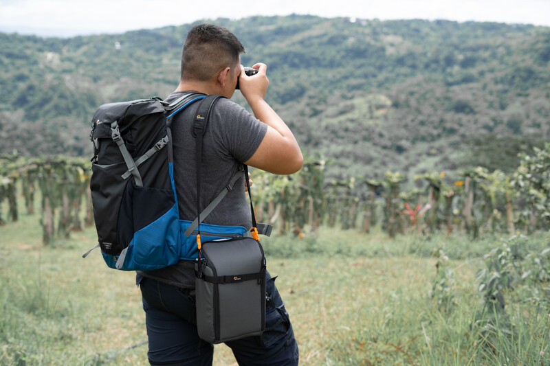 Hiker with backpack photographing mountainous landscape with valley and vegetation below.