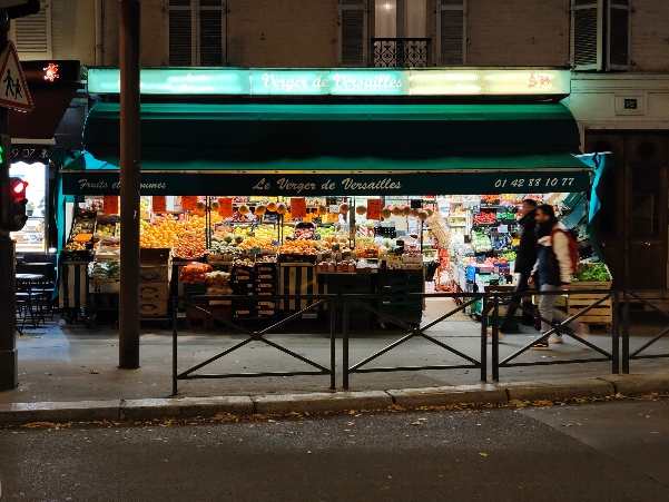 Nighttime street photography of a brightly lit flower shop storefront with turquoise awning and window displays.
