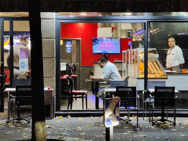 Street-level view through storefront windows of a music studio with pianos and people inside.