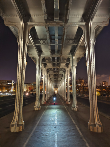 Symmetrical perspective view under a bridge at night with concrete pillars and wet pavement.
